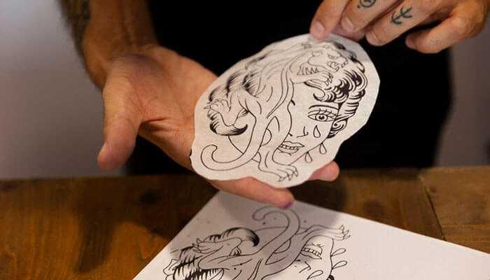 Water based adhesives - tycoonstory | tycoonstory media Custom die cut stickers featuring a woman's face with animal elements held by a tattoo artist over a table with sketches.