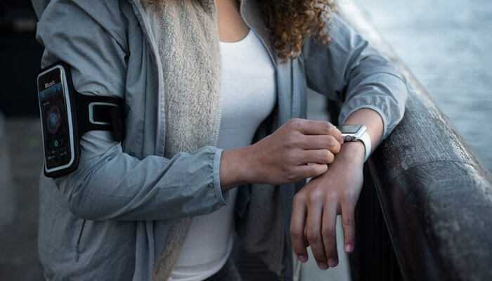 Wearable health devices - tycoonstory | tycoonstory media A woman wearing healthcare wearable devices with a gray background and it represents healthcare digital transformation.