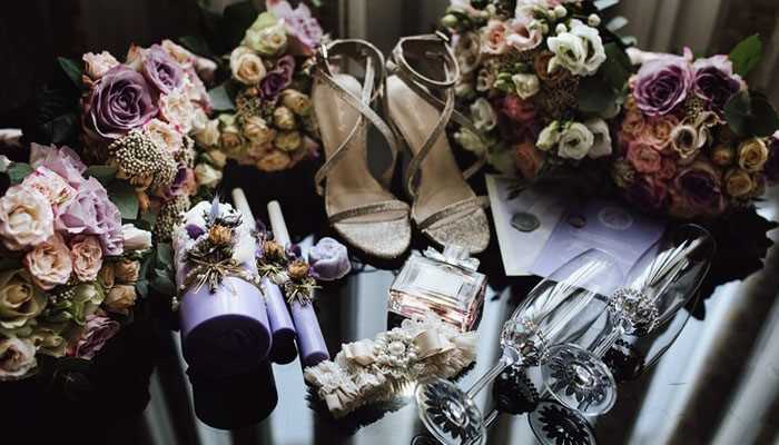 Witchy wedding in dark colors - tycoonstory | tycoonstory media Wedding themes perfect for winter elegant bridal accessories with sparkling heels floral bouquets purple accents perfume bottle crystal glasses and garter on a black surface