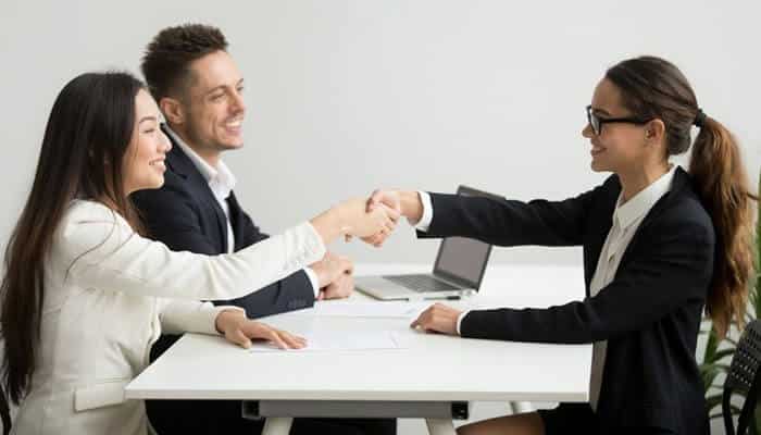 Advantages of owning a recruitment agency franchise - tycoonstory | tycoonstory media A handshake between professionals in a recruitment franchises setting, with a man and woman seated at the table