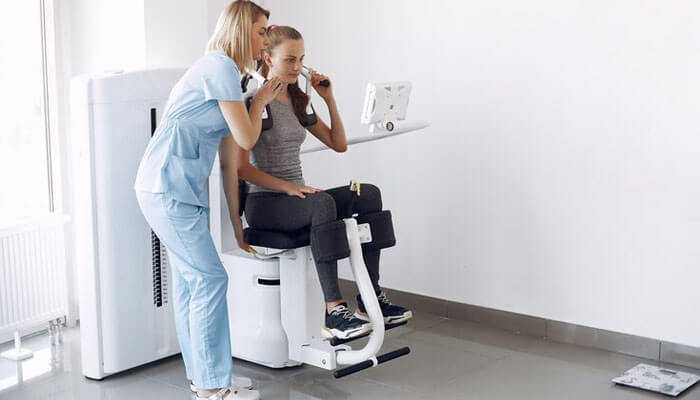 Affordability - tycoonstory | tycoonstory media Healthcare professional assisting a patient using a sit-to-stand manual lifts in a clean, well-lit clinical environment, highlighting comfort, safety, and mobility support.
