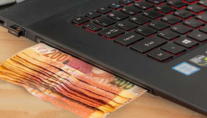 Asian handicaps - tycoonstory | tycoonstory media A stack of currency notes partially tucked under the keyboard of a laptop-a representation of soccer betting online.
