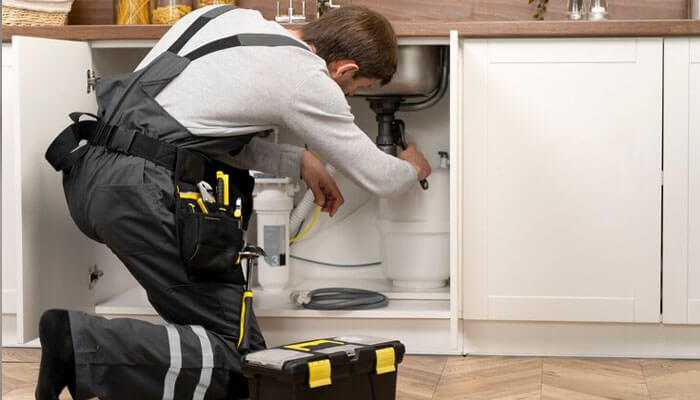 Choosing the right commercial plumbing service in san diego - tycoonstory | tycoonstory media Commercial plumbers in san diego repairing plumbing under a kitchen sink with tools and a black and yellow toolbox nearby