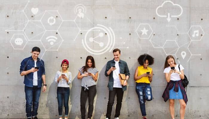 Creating youth-friendly digital spaces - tycoonstory | tycoonstory media Six youth are using smartphones by a wall with digital icons highlighting social media impact on mental health.