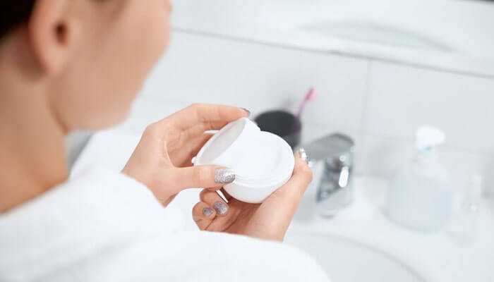 Dermatologists recommended scar clearing creams - tycoonstory | tycoonstory media A person holding a white container of scar clearing creams in a bathroom, symbolizing self-care and skincare routines