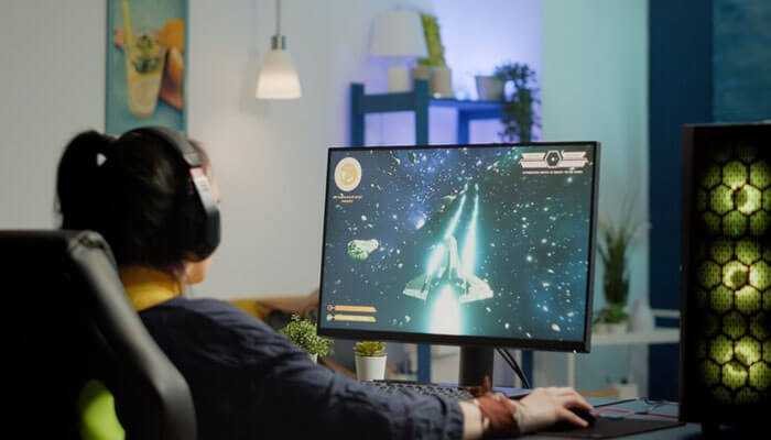 Display excellence - tycoonstory | tycoonstory media Person with headphones on playing a space video game on a desktop, showing the rise of ai powered gaming laptops.