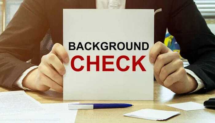 Employee background checks - tycoonstory | tycoonstory media A professional holding a placard showing employee background checks, with documents and a pen on the desk.