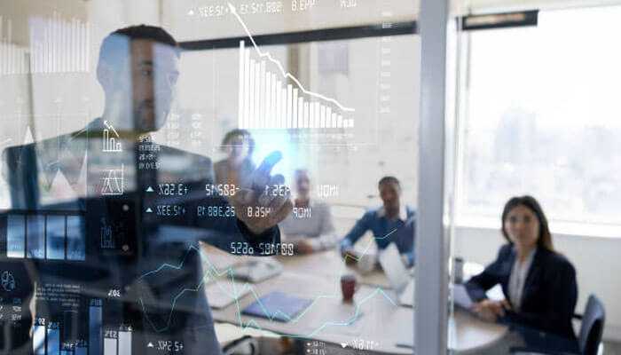 Future trends in investment training - tycoonstory | tycoonstory media A business person demonstrating financial data on a clear screen to a team representative for companies offering investment training.