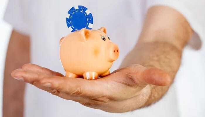 How to make the most of low deposits - tycoonstory | tycoonstory media A person holding a piggy bank with a blue poker chip inserted, symbolizing savings and minimum deposit casinos.