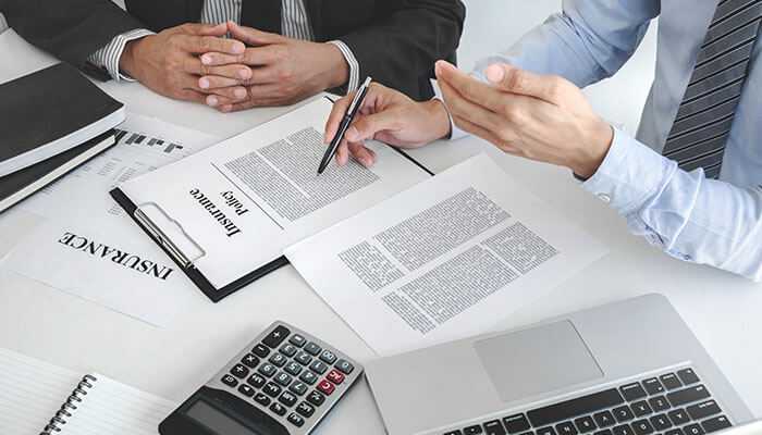 How to select the best policy for your needs - tycoonstory | tycoonstory media Us health insurance business professionals reviewing insurance policy documents at a desk with a laptop calculator and paperwork in a formal office setting