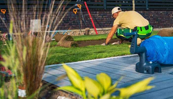 Landscape design and installation - tycoonstory | tycoonstory media Landscaping business worker laying fresh sod on a lawn with landscaping tools in the background, emphasizing outdoor landscaping and maintenance work.