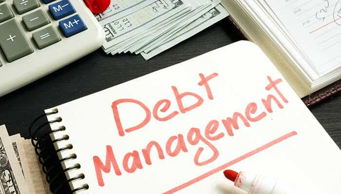 Make debt management easier - tycoonstory | tycoonstory media A notebook with debt management written in bold red letters, surrounded by a calculator, money, and documents, symbolizing fintech solutions for financial planning and control