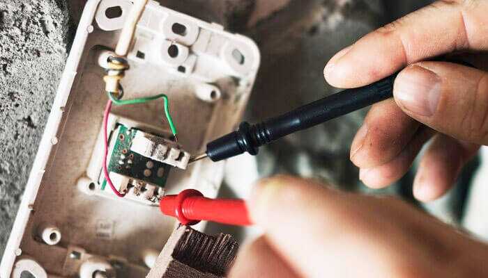 Matching connectors to applications - tycoonstory | tycoonstory media Hands testing electrical connectors with a multimeter on a wall-mounted wiring setup.