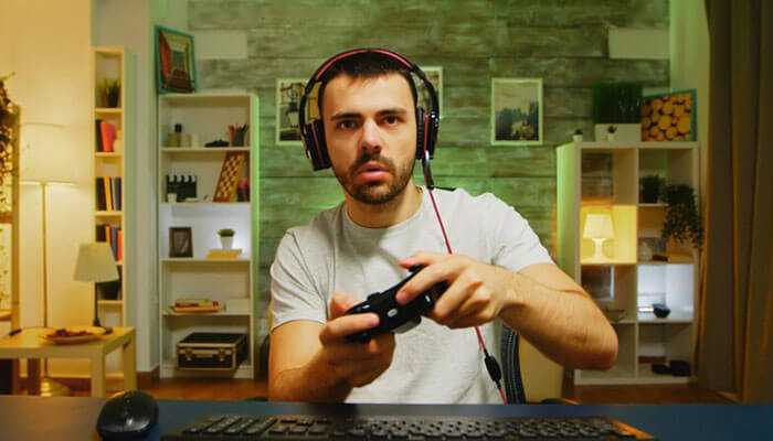 Multi-device support - tycoonstory | tycoonstory media A man with a gaming headset holding a controller, playing games like html5 slot machines in a cozy room setup.