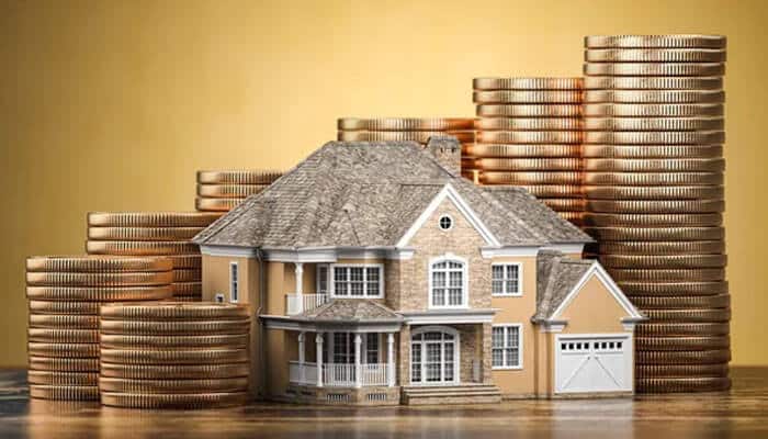 Overestimating the property value - tycoonstory | tycoonstory media A miniature house surrounded by stacks of gold coins, symbolizing real estate investment and property financing.