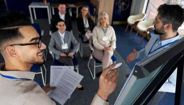 Potential drawbacks of real estate seminars - tycoonstory | tycoonstory media A man stands at a whiteboard while presenting real estate investment seminars to a seated audience in a modern conference room.