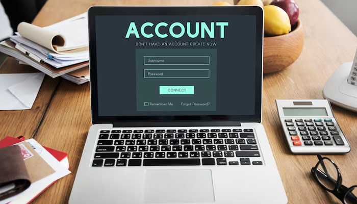 Setting up your micro-investing account - tycoonstory | tycoonstory media Laptop displaying a micro-investing account login screen on a workspace desk with a calculator, papers, and a pen