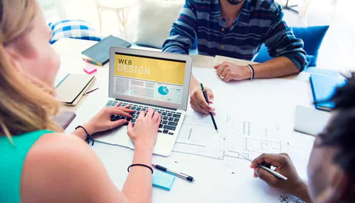 Sustainable web design - tycoonstory | tycoonstory media Team collaborating on a website redesign project, emphasizing why your website needs an update, with a laptop displaying'Web Design' and design sketches on the table