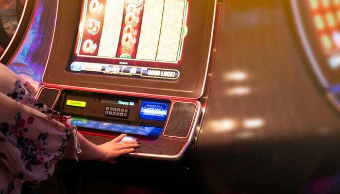 Testing and optimization - tycoonstory | tycoonstory media A person playing on a casino slot machine with colorful screens and bright lighting, focusing on his hand touching the buttons.