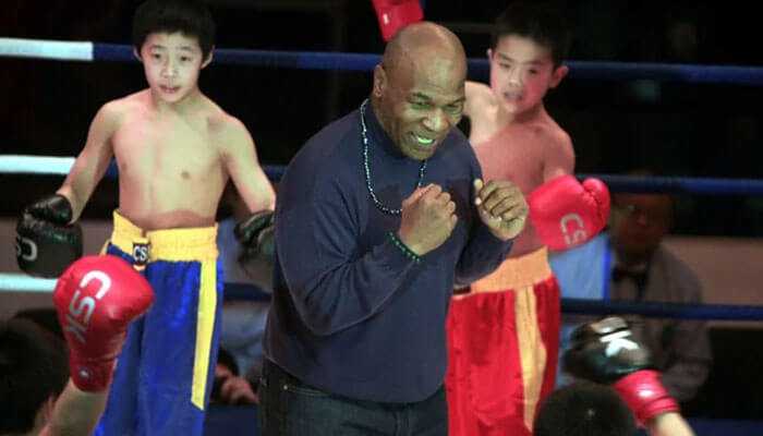 The influence of mike tysons fight legacy - tycoonstory | tycoonstory media Mike tyson laughing and interacting with young boxers in the ring, reflecting his ongoing influence in the boxing world and his successful career contributing to his net worth.