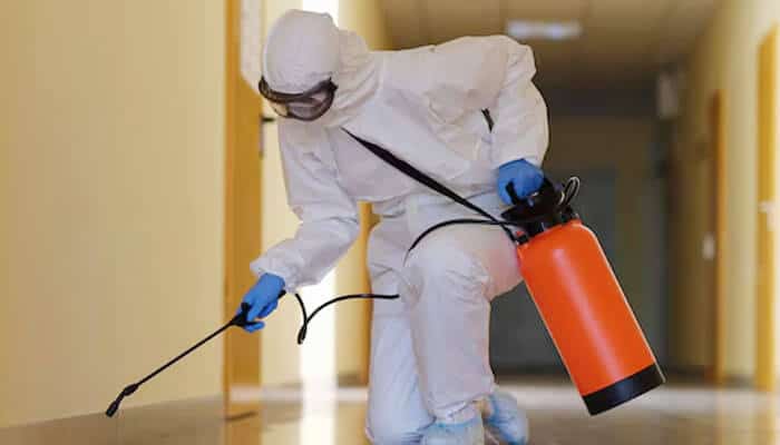The role of professionals in mold remediation | tycoonstory media The picture depicts a person in protective gear using an orange sprayer to sanitize or decontaminate an indoor hallway, probably for mold remediation or pest control.