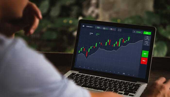 Using option greeks for strategic advantage - tycoonstory | tycoonstory media Person analyzing a stock market trading graph on a laptop screen, featuring a candlestick chart, option greeks data, and buy/sell buttons in a calm, outdoor setting