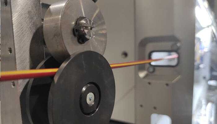 Versatility in material applications - tycoonstory | tycoonstory media The image shows a closeup of a profile wrapping machine, with cylindrical rollers guiding a thin material or wire through the process in an industrial setting