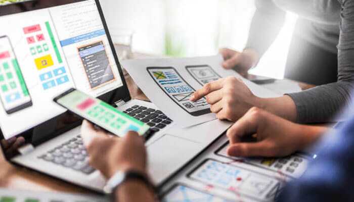 Why invest in digital product design services - tycoonstory | tycoonstory media Designers working on digital product design services, reviewing wireframes, and testing user interfaces on devices.