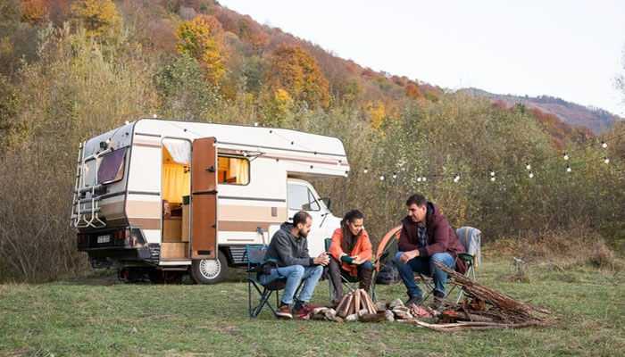 Benefits of caravan ownership - tycoonstory | tycoonstory media Friends having fun around a campfire near their caravan in autumn, made possible by caravan finance in australia.