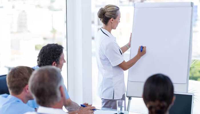 Professional woman explaining on the whiteboard cross-contamination in medical environments to her colleagues attending the meeting.