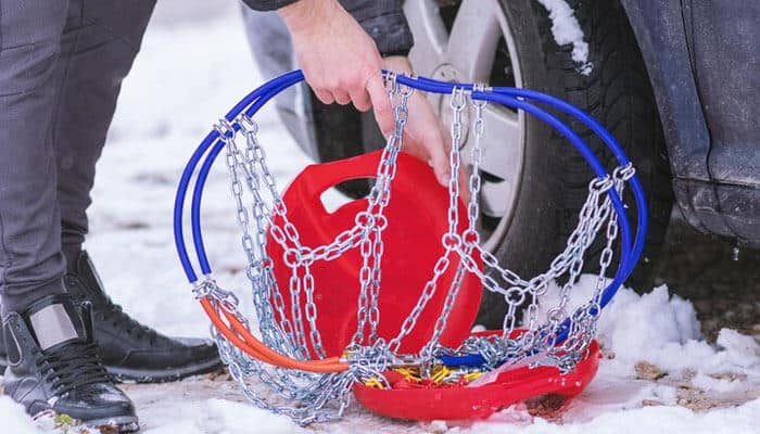 Educational support - tycoonstory | tycoonstory media Person holding snow chains near the tire of a car, in snow, depicting following passenger vehicle chain laws.