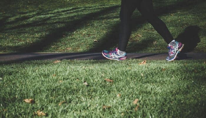 Exercise - tycoonstory | tycoonstory media A person walking on a paved path surrounded by grass, wearing colorful running shoes and black leggings, promoting an active lifestyle to prevent osteoporosis