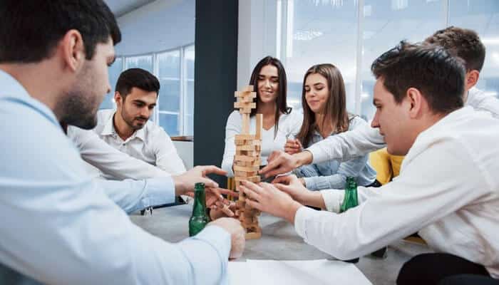How rituals build employee engagement and morale - tycoonstory | tycoonstory media Team playing jenga during a team-building activity in the office, fostering collaboration and custom traditions in entrepreneurship.