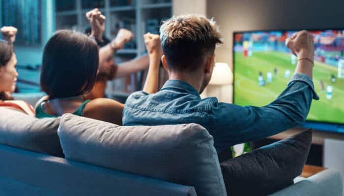How to improve the streaming experience on streameast - tycoonstory | tycoonstory media A group of friends watching a live sports match on tv, celebrating together, with a clear focus on the excitement of streaming sports content on streameast.