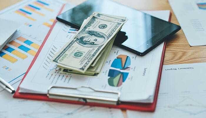 Investments and business ventures - tycoonstory | tycoonstory media Kylian mbappe net worth stack of dollar bills on financial reports with charts and a tablet