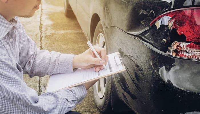 Litigation and court proceedings - tycoonstory | tycoonstory media An insurance adjuster inspects a damaged car and makes notes on a clipboard, as shown in the car accident claims process.
