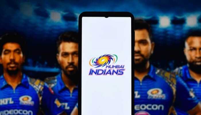 Mumbai indians - tycoonstory | tycoonstory media The image highlights ipl 2025, featuring the mumbai indians logo on a smartphone with players in iconic jerseys against a vibrant stadium backdrop.
