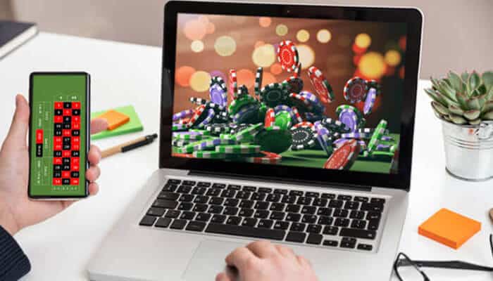 Online casino - tycoonstory | tycoonstory media A person uses a smartphone for roulette and a laptop displaying virgin games casino chips on a desk.