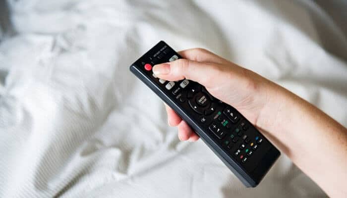 Pairing the remote control - tycoonstory | tycoonstory media A person holding a black tv remote control, possibly for an amazon fire stick, while sitting on a bed with a white bedsheet