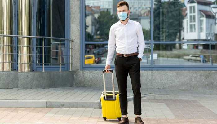 Promoting safe tourism A man with a yellow suitcase and mask in an urban setting, emphasizing the need for travel insurance.