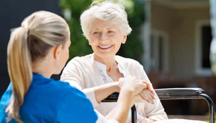 The art of active listening in healthcare settings - tycoonstory | tycoonstory media Elderly woman in a wheelchair smiling at a caregiver, highlighting compassion and assisted living course