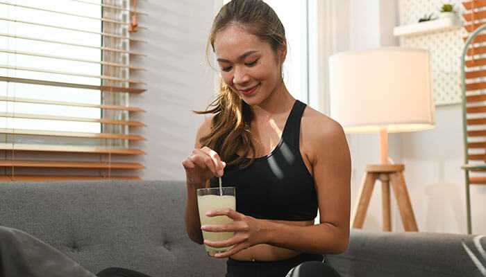 Types of collagen for bone health - tycoonstory | tycoonstory media Young woman in activewear stirring a glass of collagen supplements drink while sitting on a couch, promoting bone health