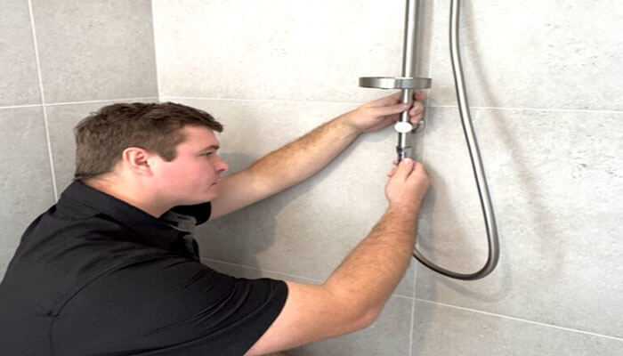 4 services your local plumber can assist you with - tycoonstory | tycoonstory media A professional local plumber repairing a shower fixture, adjusting the water connection in a modern tiled bathroom