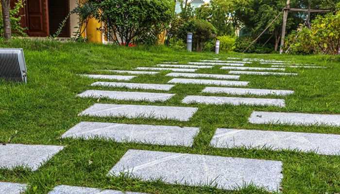Garden steps are also a good option - tycoonstory | tycoonstory media A landscaper-designed garden pathway with staggered stone pavers on a lush lawn, surrounded by greenery and outdoor lighting.