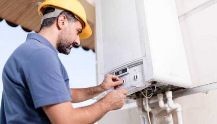 Gas heating service and repair - tycoonstory | tycoonstory media Technician wearing a yellow hard hat adjusting a wall-mounted boiler system, representing plumbing diy jobs.