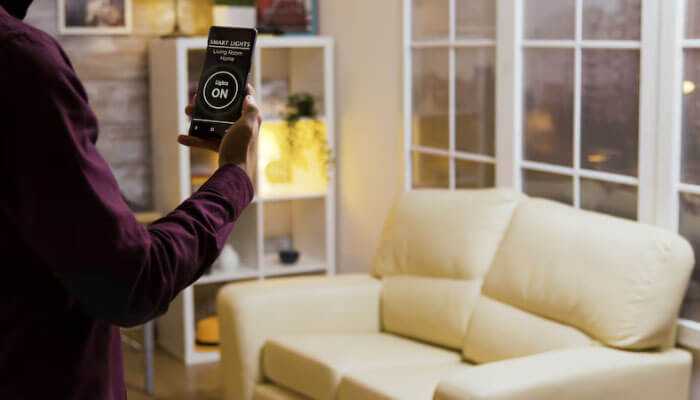 Home automation in the design phase - tycoonstory | tycoonstory media A person controlling smart lights using a smartphone demonstrates home design with tech in a living room.