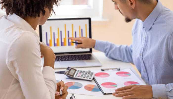 Implementing investment strategies - tycoonstory | tycoonstory media Two financial advisors analyzing investment charts and data on a laptop, discussing strategies for a balanced investment portfolio.