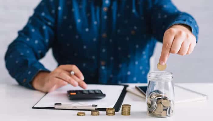 Key benefits of using a personal loan emi calculator - tycoonstory 1 | tycoonstory media Person calculating savings and loan payments using an emi calculator with coins and a calculator on the table