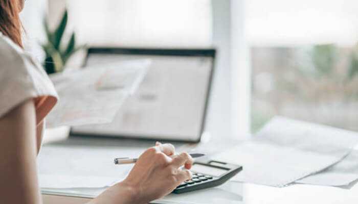 Predictive analytics for improved payment forecasting - tycoonstory | tycoonstory media A person uses a calculator while holding a document, with a laptop and papers in the background, suggesting swift payment tracking and financial work.