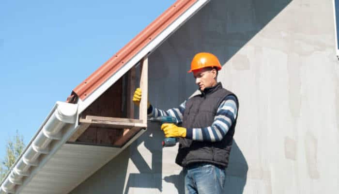 Repairing timber fascia and eaves - tycoonstory | tycoonstory media Construction worker in safety helmet and gloves repairing house roof, pointing out key roof treatments for maintenance.